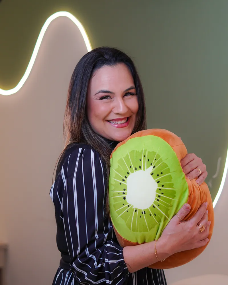 Juliana Araújo sorrindo com uma almofada de kiwi