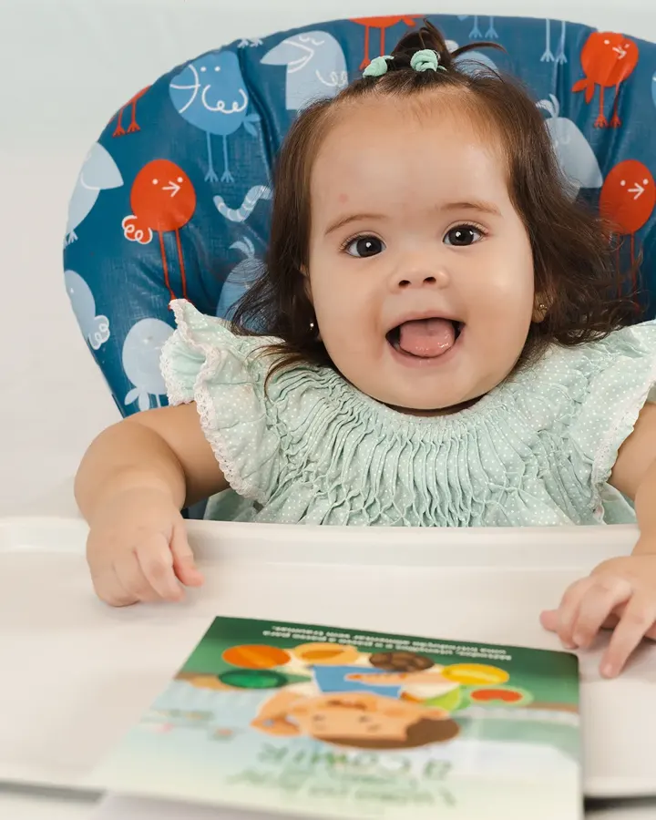 Bebê sorrindo na cadeira de alimentação com o livro